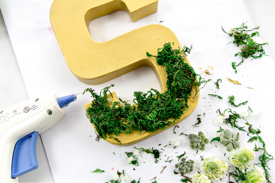 a paper mache letter painted gold and being decorated with moss