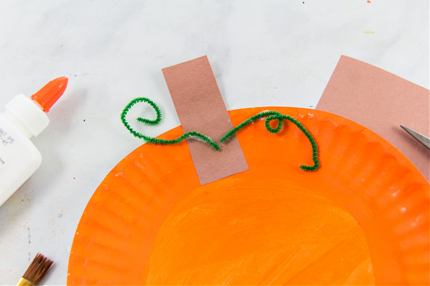 a green pipe cleaner vine glued to a paper plate pumpkin