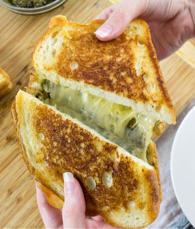 hands stretching a grilled cheese with pesto sandwich