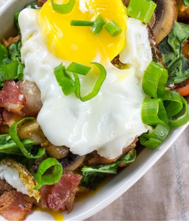 tater tots topped with breakfast items including egg, sausage, bacon, mushrooms, tomato, and spinach