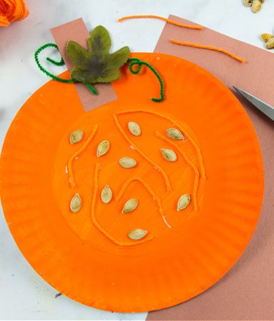 a paper plate pumpkin craft that teaches kids the parts of a pumpkin including seeds and fibrous strands.