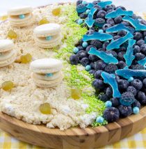ocean themed charcuterie board with rice krispies sand, macaron clams, blueberry and gummy ocean with gummy sharks