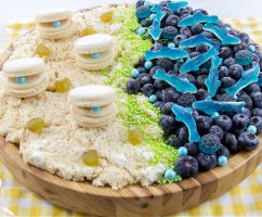 ocean themed charcuterie board with rice krispies sand, macaron clams, blueberry and gummy ocean with gummy sharks