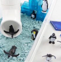 winter sensory bin with a tube slide, magnetic blocks, blue sand, and penguins.