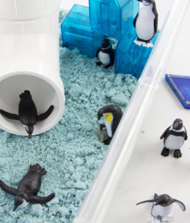 winter sensory bin with a tube slide, magnetic blocks, blue sand, and penguins.