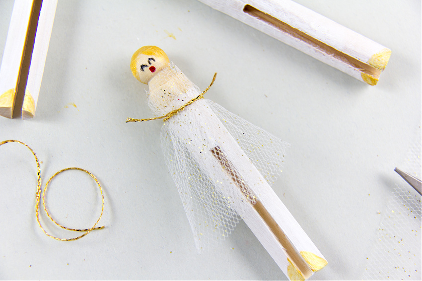 a clothespin angel painted white and gold with tulle wrapped around it