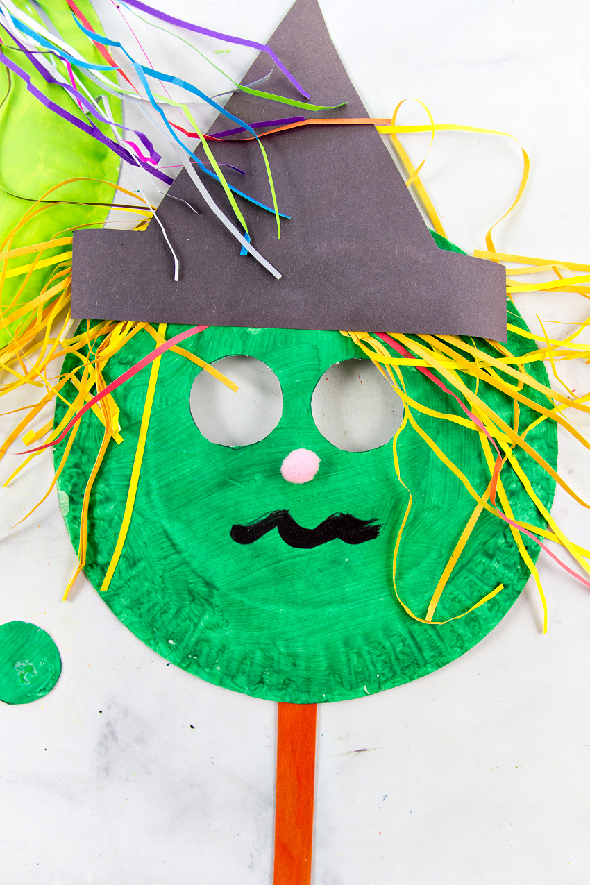 a colorful paper plate witch mask with shredded paper hair and a pom pom nose