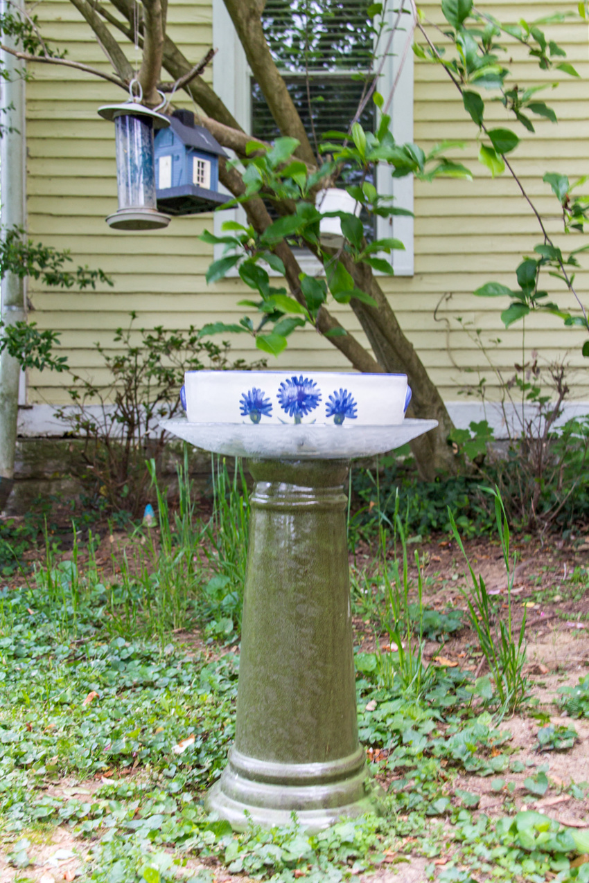 a green blue and white diy bird bath with painted flowers in a garden