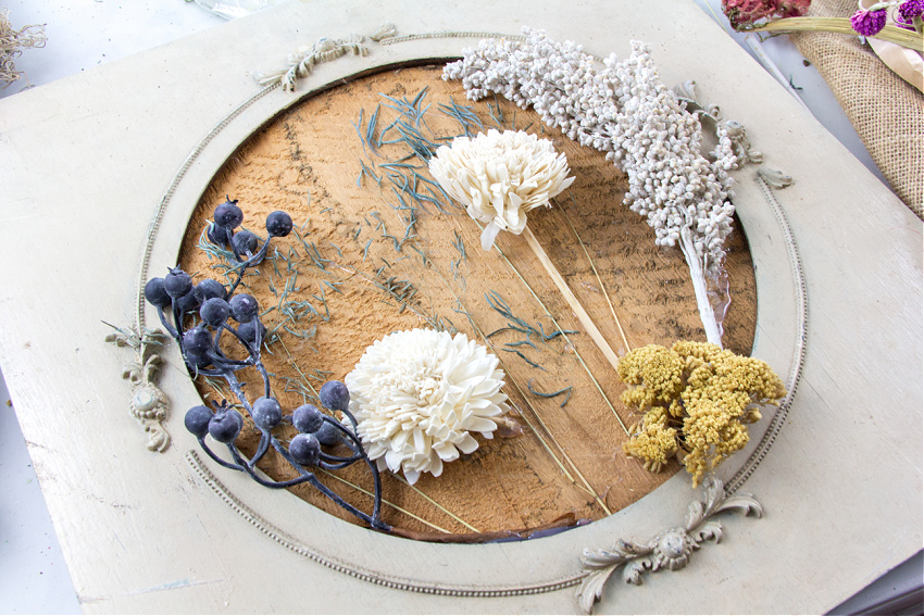dried flowers and faux dried flowers being arranged on a frame to hang on the wall.