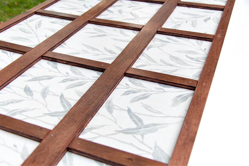 wood cut to resemble windows over wallpaper attached to a wood headboard