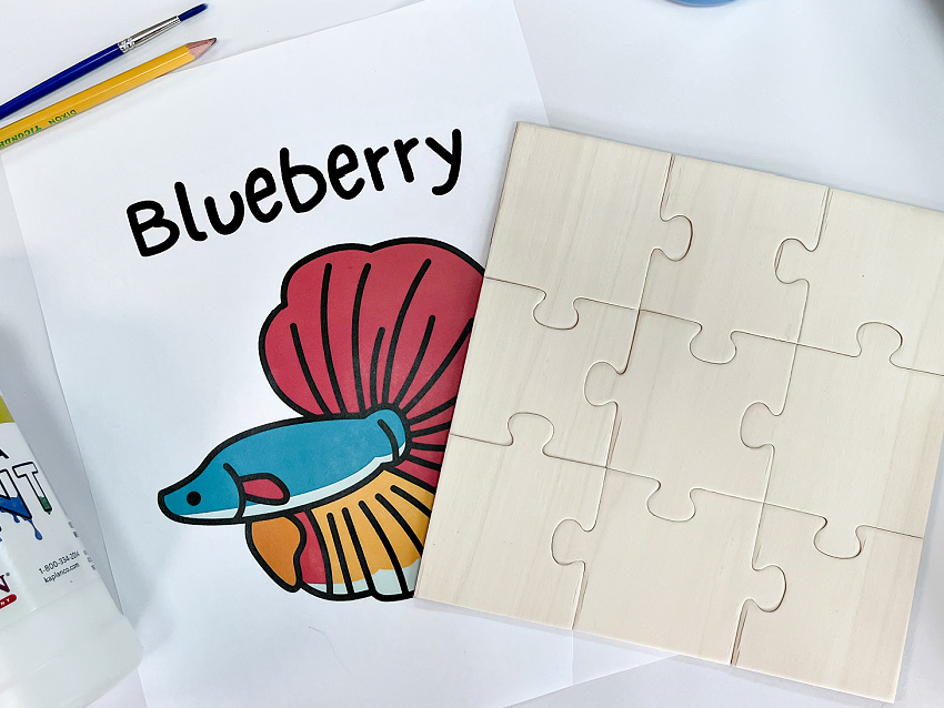 a diy wood magnet puzzle with a picture of a betta fish, pencil, paint, and paintbrush