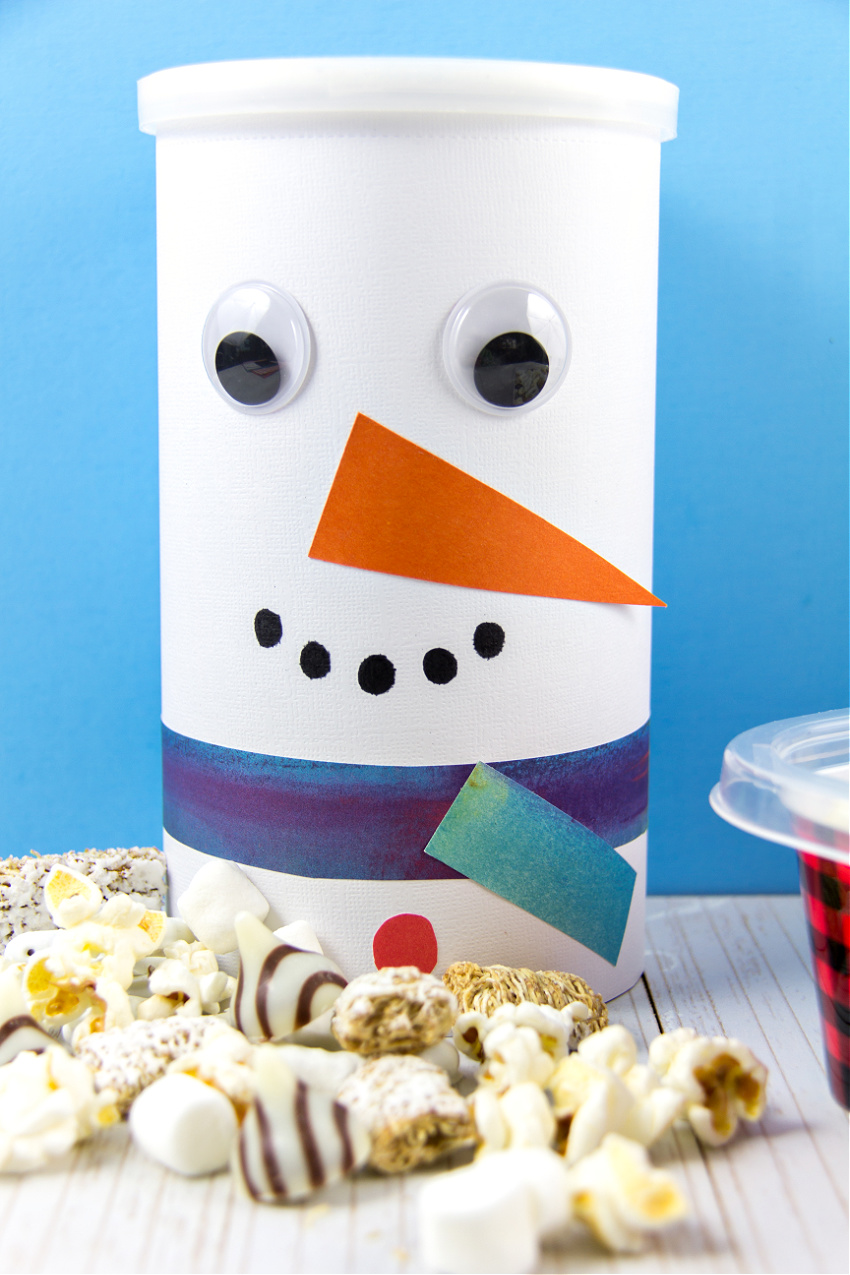 an oatmeal container turned into a diy snowman container filled with snowman snack mix for winter
