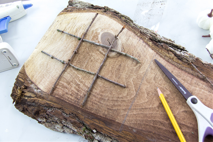 a wood slice and twigs used to make a diy tic tac toe board