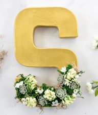 paper mache letter s decorated with moss, faux succulents, and faux flowers
