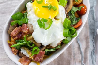 tater tots topped with breakfast items including egg, sausage, bacon, mushrooms, tomato, and spinach