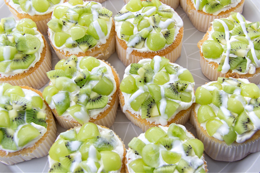 a tray of mini angel food cakes topped with green grapes and kiwi fruit