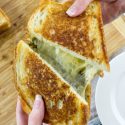 hands pulling apart a grilled cheese with pesto sandwich
