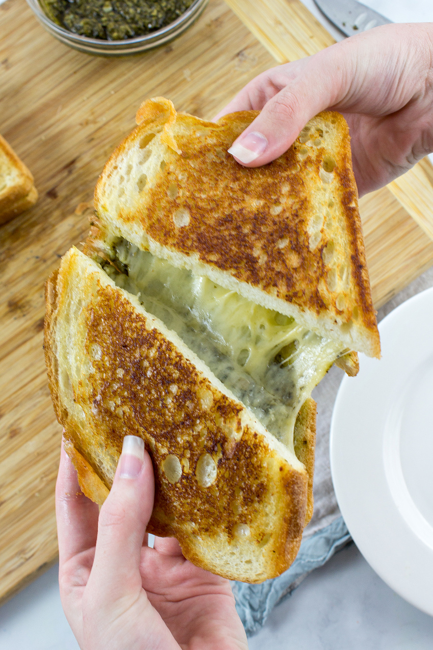 hands pulling apart a grilled cheese with pesto sandwich