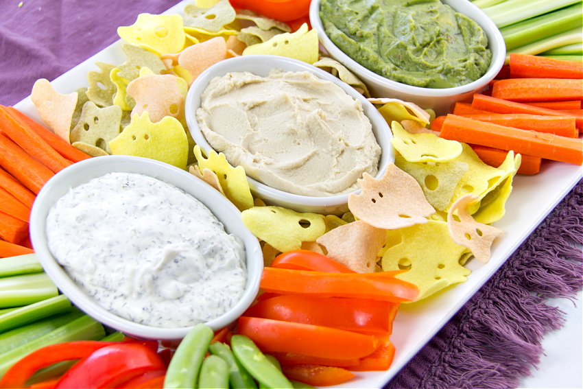 3 bowls of dips surrounded by ghost and bat chips and healthy halloween snacks