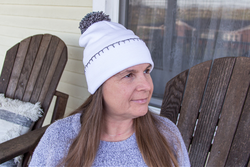 a white beanie with grey embroided blanket stitch and a grey pom pom attached