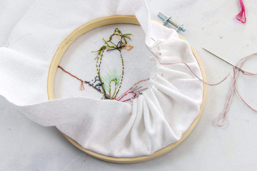 Finish off the back of an embroidery hoop by stitching lightly and then pulling the stitches tight to gather the fabric into the center of the hoop