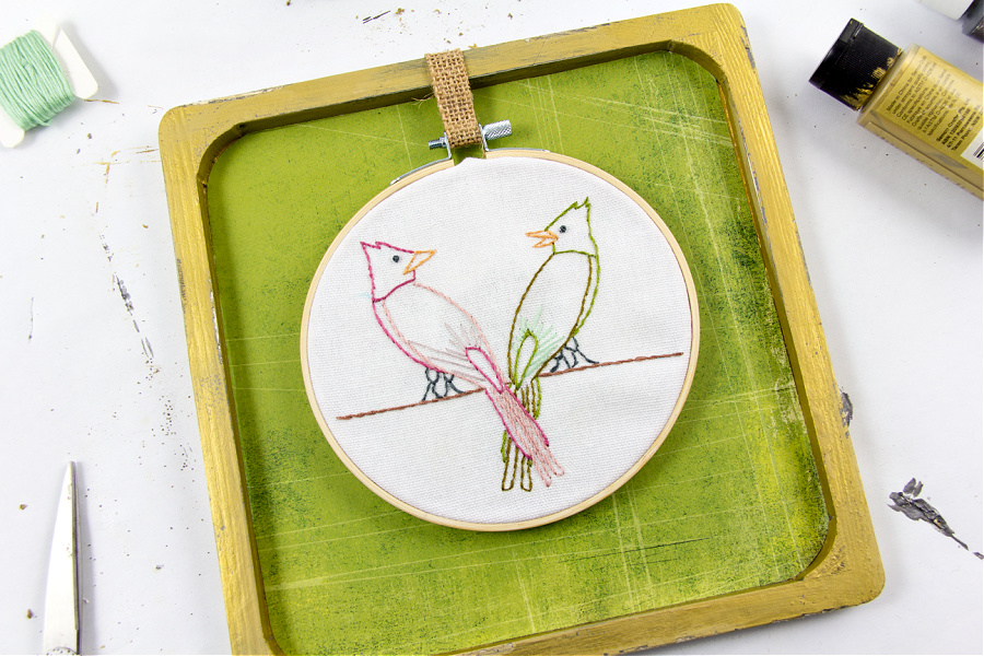 an embroidery hoop hanging in a plain wood frame with burlap