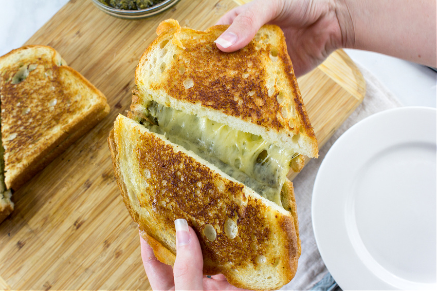 hands stretching a grilled cheese with pesto sandwich 