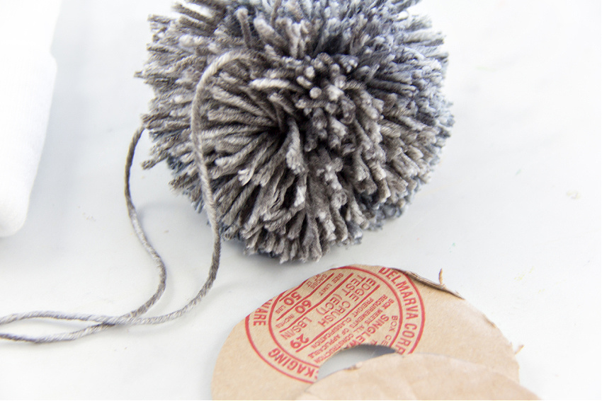 a grey yarn pom pom made for a beanie using two cardboard rings