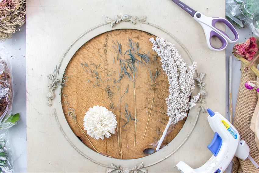 a dried flower wall art piece being made using a large antique frame and assorted dried and faux dried flowers.
