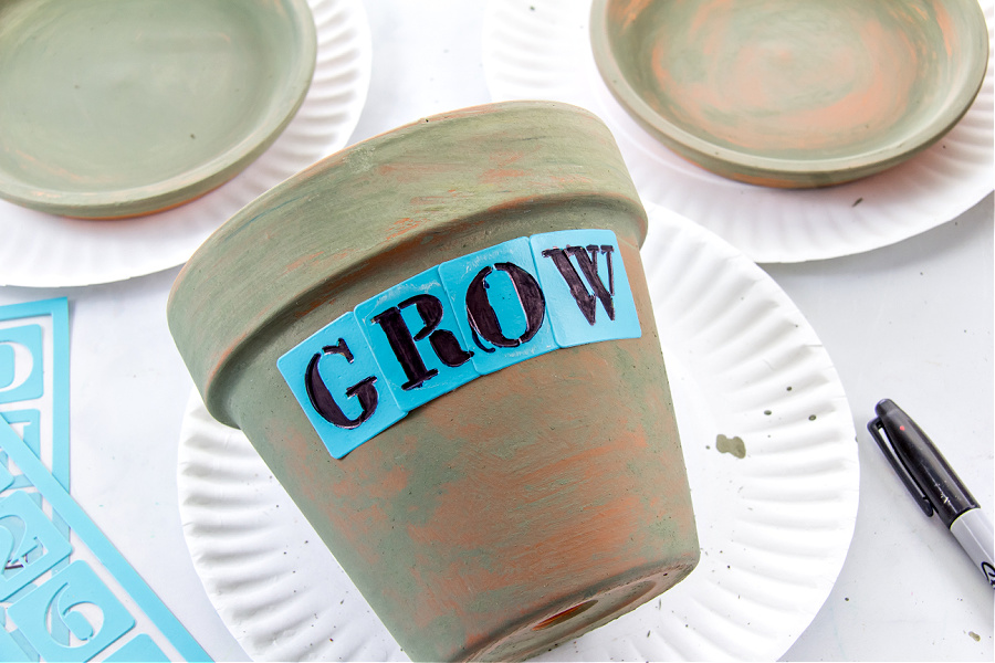 a stencil and permanent marker being used on a terracotta pot