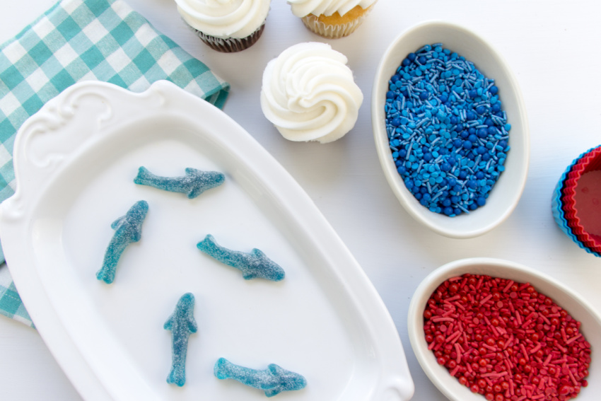 use store bought cupcakes, blue and red sprinkles and gummy sharks to make shark cupcakes