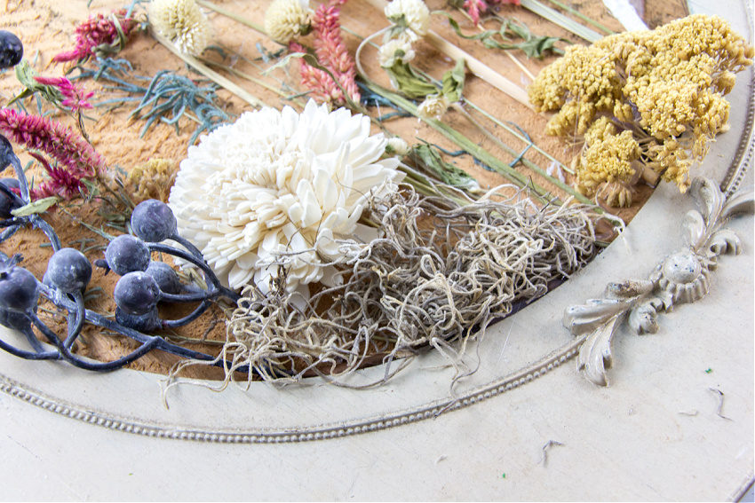spanish moss being used to fill gaps and cover glue on a dried flower wall art arrangement
