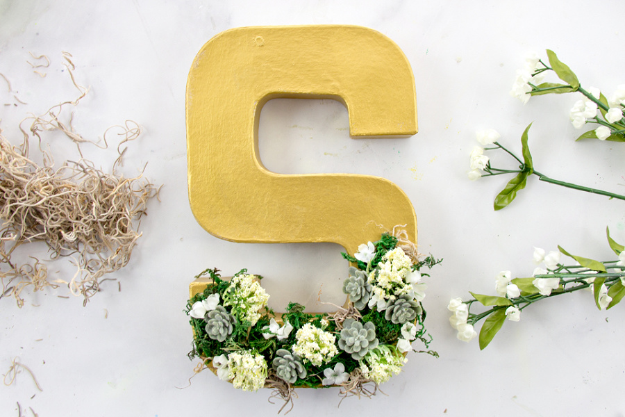 paper mache letter s decorated with moss, faux succulents, and faux flowers
