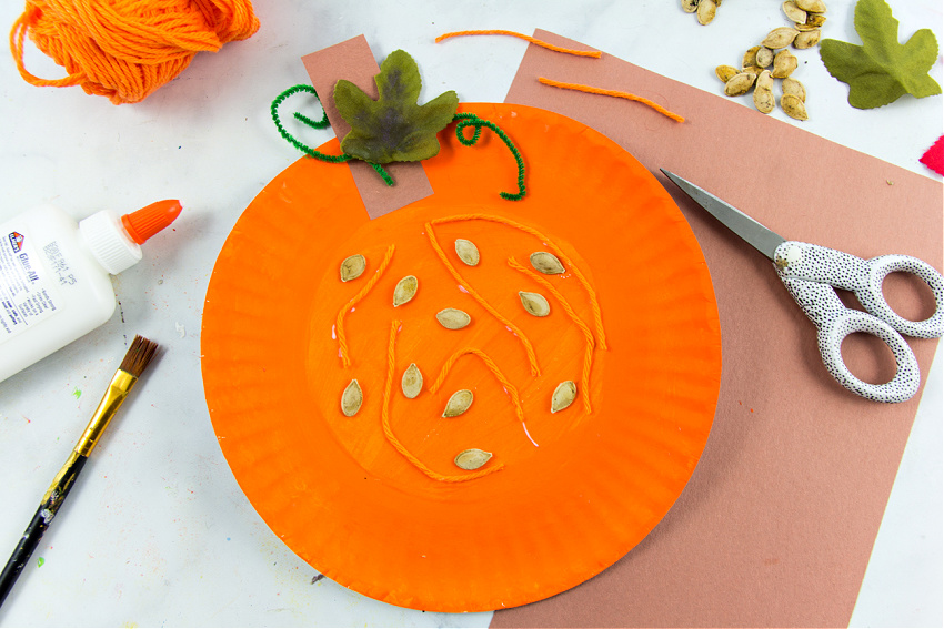 a paper plate pumpkin craft that teaches kids the parts of a pumpkin including seeds and fibrous strands.