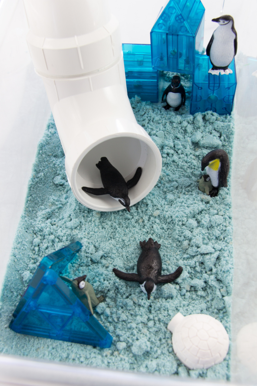 blue sand in a tub with magnetic blocks, penguins, and a plumbing tube slide