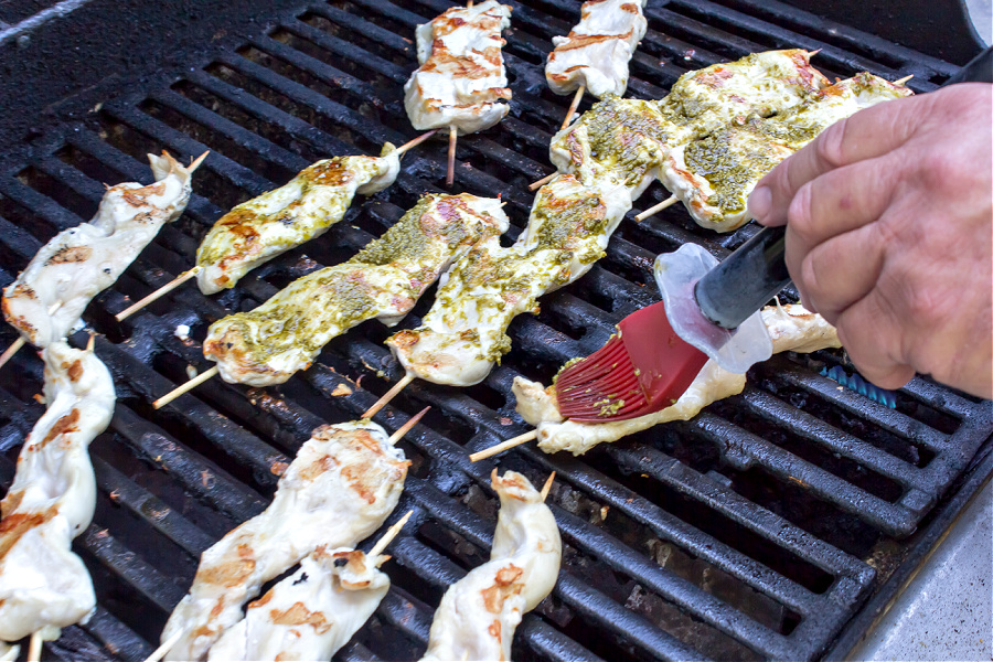 chicken kabobs being brushed with pesto and cooked on the grill