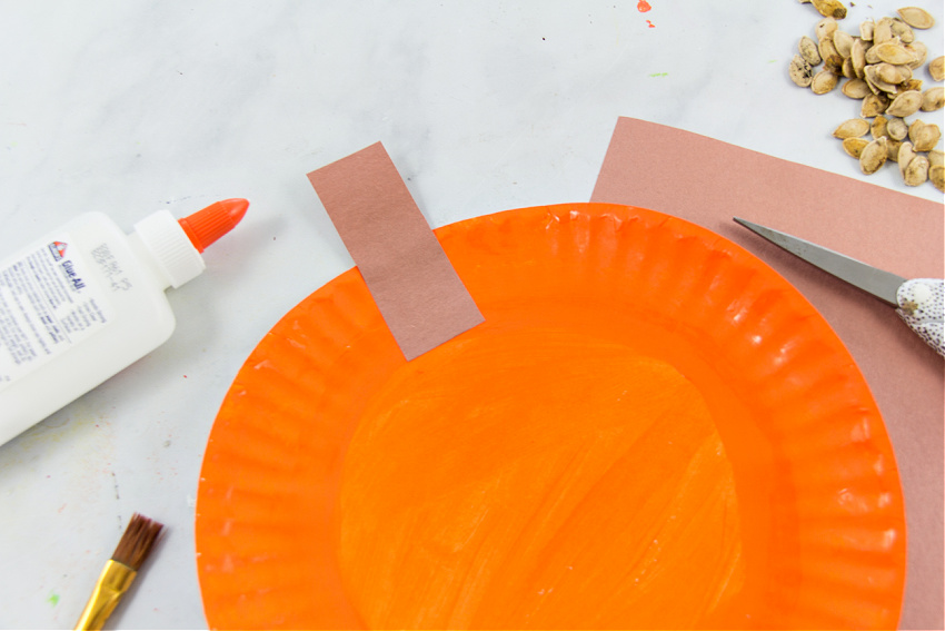 a brown construction paper stem attached to a paper plate painted orange