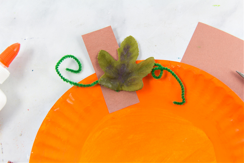 a paper plate pumpkin with a paper stem, pipe cleaner vines, and plastic leaf.