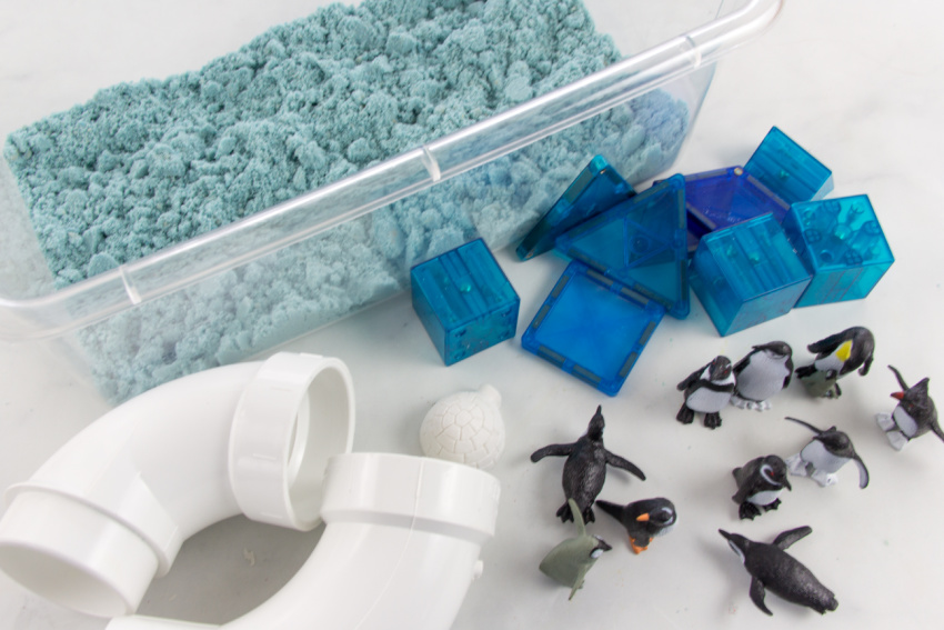 gather a tub, blue sand, penguins, magnetic blocks, a plumbing tubes for a penguin sensory bin