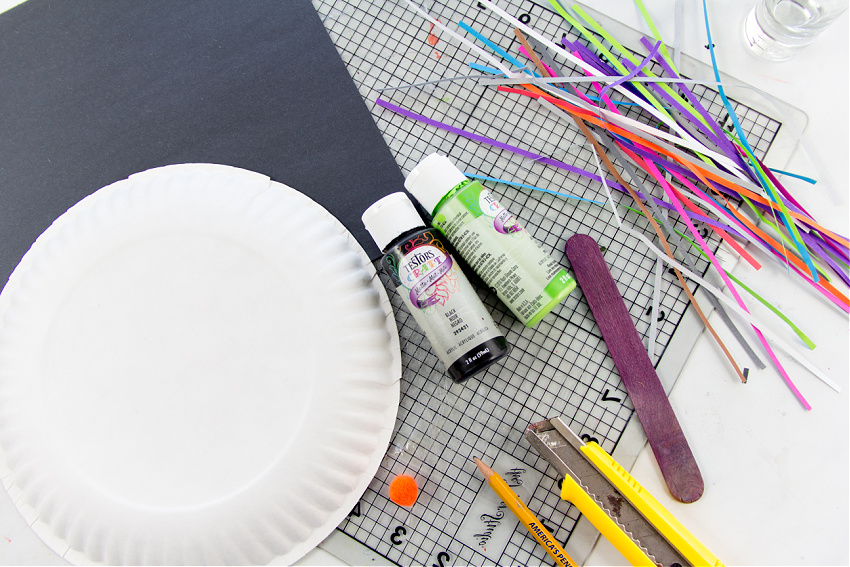 You need a paper plate, construction paper, craft stick, box cutter, and paint to make a paper plate witch mask