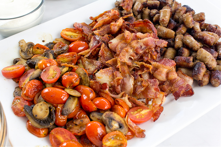 tomato, mushrooms, bacon, and sausage on a tray to make a recipe for loaded tater tots