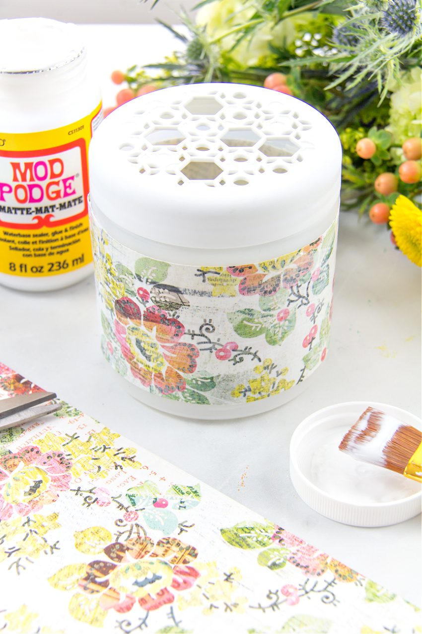 an odor eliminator container wrapped in pretty scrapbook paper to turn it into a spring vase