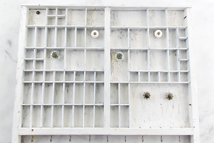 printers typeset tray painted white with knobs added for hanging things.