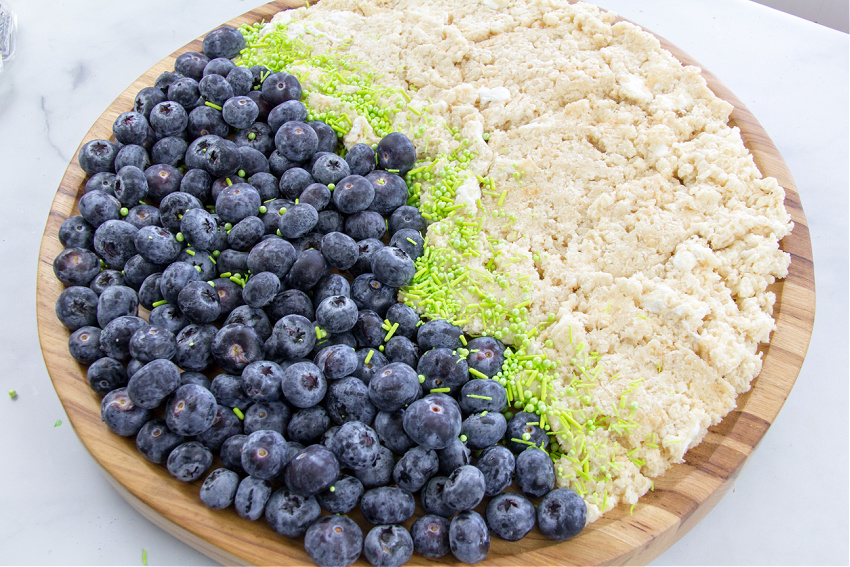 a round charcuterie with rice krispies sand on one side and blueberries water on the other for an under the sea party tray