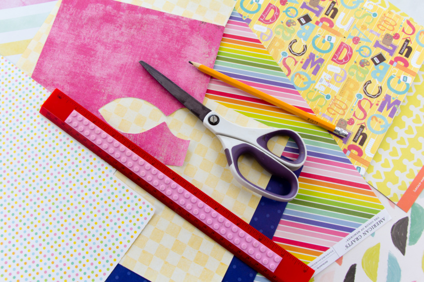 gather scrapbook paper, scissors, a ruler, and pencil to make squares for a kindness quilt